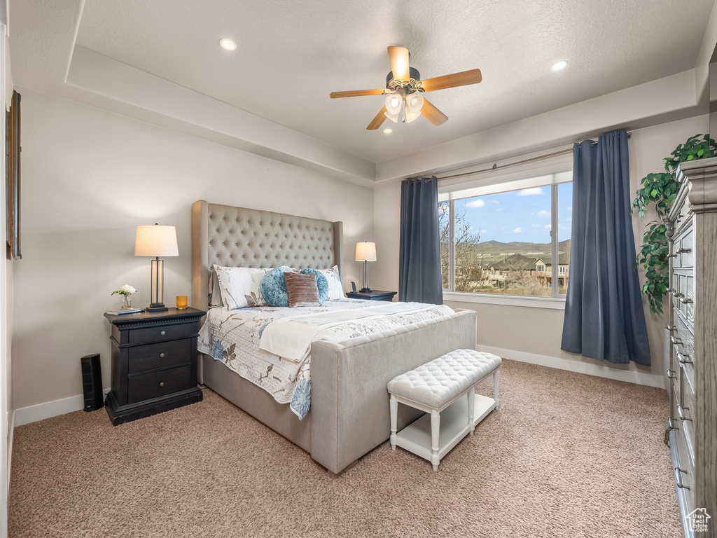 Bedroom featuring ceiling fan, light colored carpet, and a tray ceiling