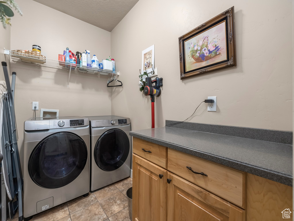 Clothes washing area with washer hookup, washing machine and clothes dryer, cabinets, and light tile flooring