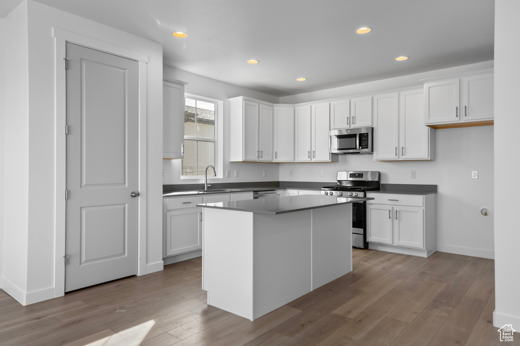 Kitchen featuring sink, light hardwood / wood-style flooring, stainless steel appliances, white cabinets, and a center island