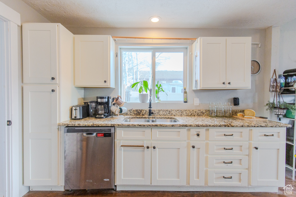 Kitchen featuring white cabinets, stainless steel dishwasher, light stone countertops, and sink