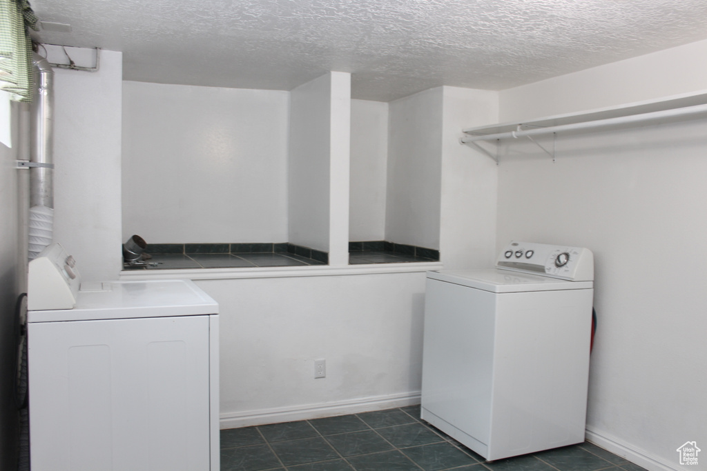 Laundry area with a textured ceiling, dark tile floors, and washing machine and clothes dryer