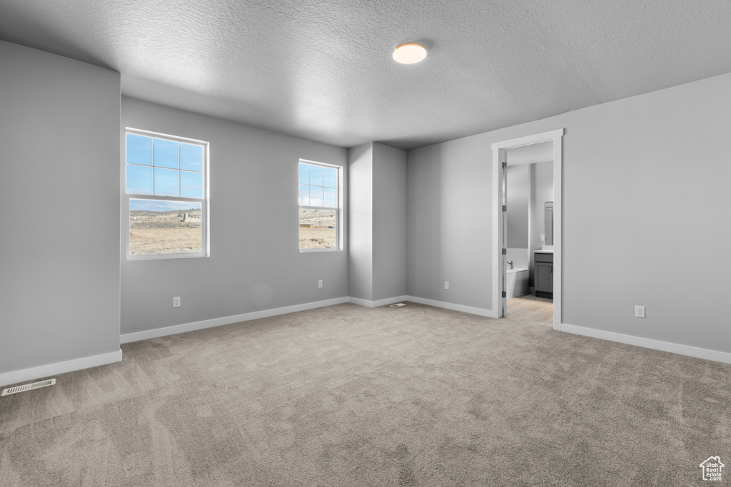 Unfurnished bedroom with light carpet, connected bathroom, and a textured ceiling