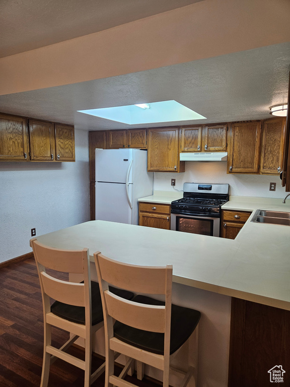 Kitchen featuring gas stove, white fridge, dark hardwood / wood-style floors, kitchen peninsula, and sink