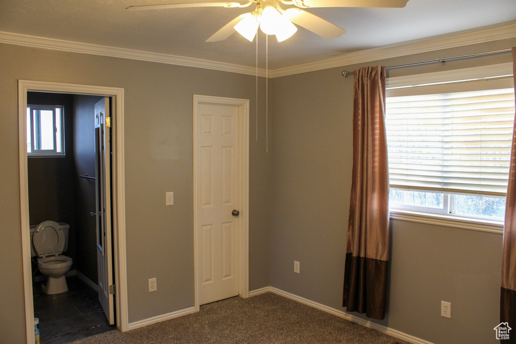 Unfurnished bedroom featuring dark carpet, connected bathroom, ornamental molding, and ceiling fan