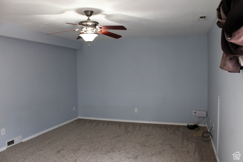 Spare room with ceiling fan and dark colored carpet