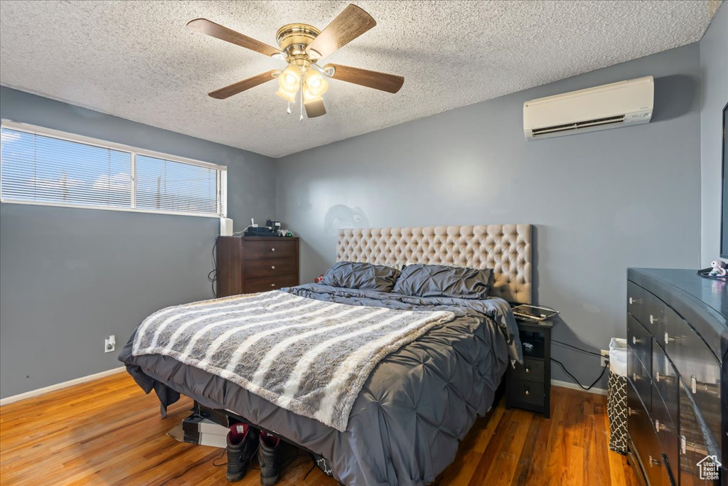 Bedroom featuring ceiling fan, a textured ceiling, a wall mounted AC, and dark hardwood / wood-style floors