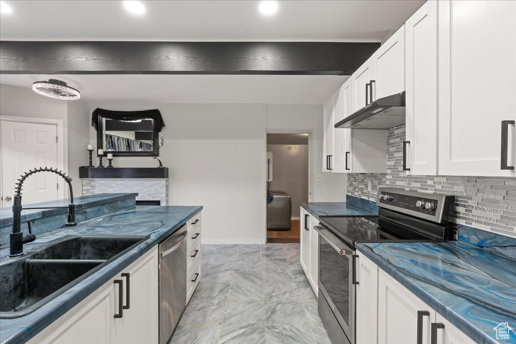 Kitchen featuring appliances with stainless steel finishes, white cabinets, light tile floors, backsplash, and sink
