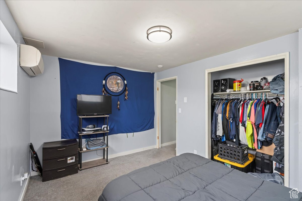 Bedroom with a closet, light colored carpet, and an AC wall unit