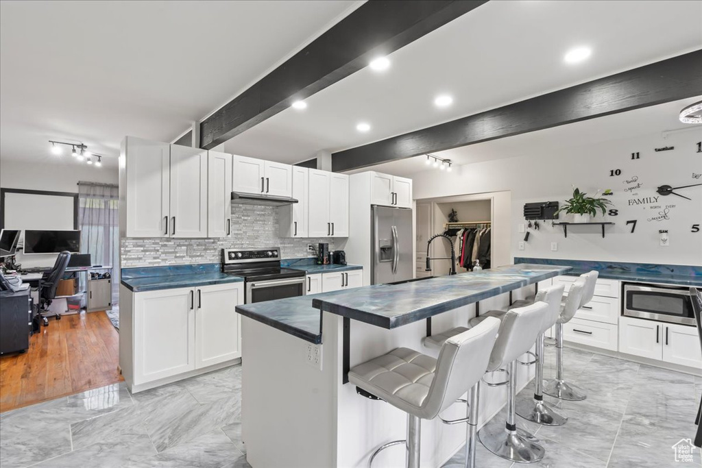 Kitchen with appliances with stainless steel finishes, beam ceiling, white cabinetry, and light tile floors
