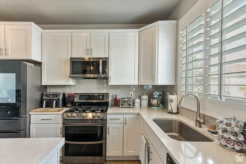 Kitchen featuring white cabinets, tasteful backsplash, sink, and stainless steel appliances