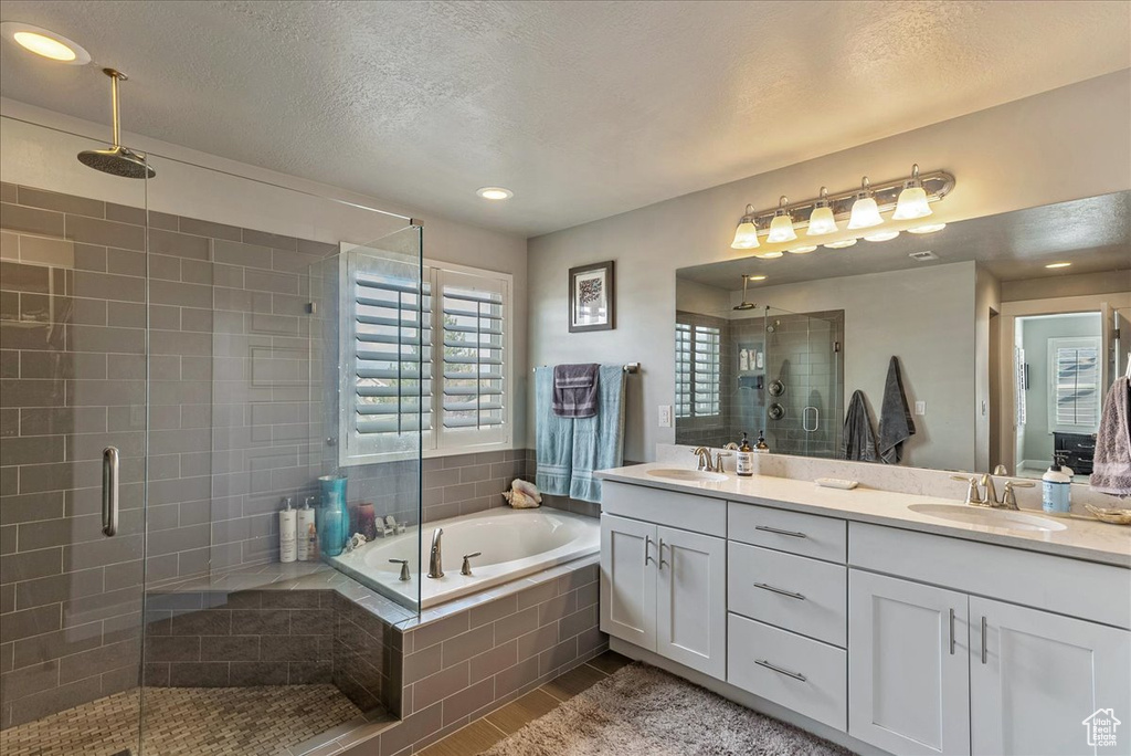 Bathroom with a textured ceiling, independent shower and bath, dual bowl vanity, and tile flooring