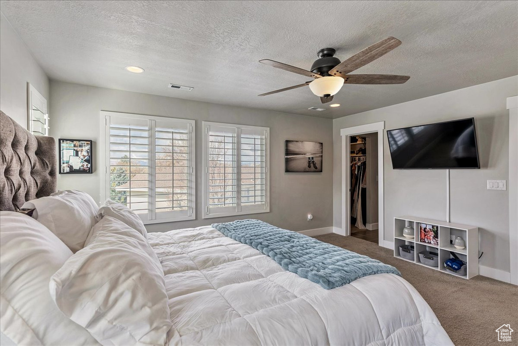 Bedroom featuring a walk in closet, ceiling fan, a textured ceiling, a closet, and light carpet