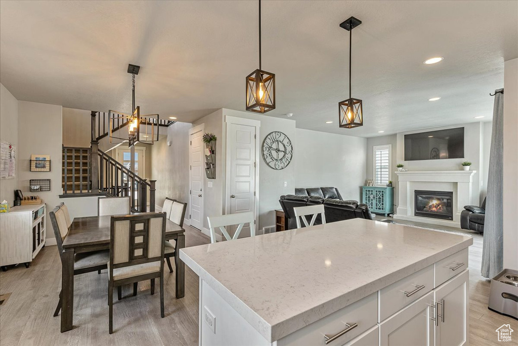 Kitchen with a notable chandelier, light hardwood / wood-style flooring, white cabinets, a kitchen island, and pendant lighting