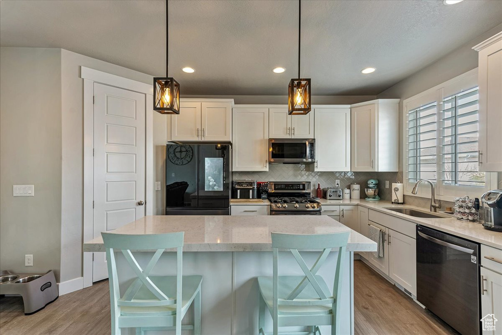 Kitchen with sink, stainless steel appliances, white cabinets, a kitchen island, and pendant lighting