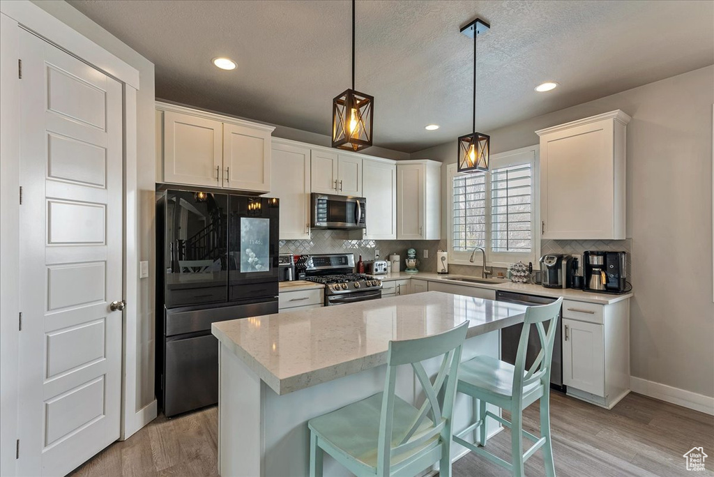 Kitchen featuring appliances with stainless steel finishes, hanging light fixtures, a center island, light hardwood / wood-style flooring, and white cabinets