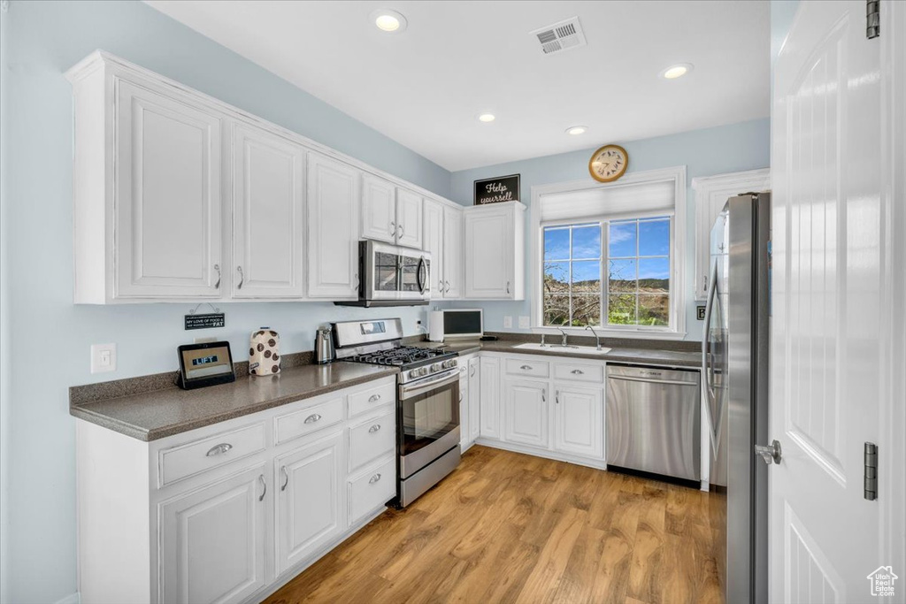 Kitchen with appliances with stainless steel finishes, sink, light hardwood / wood-style floors, and white cabinets
