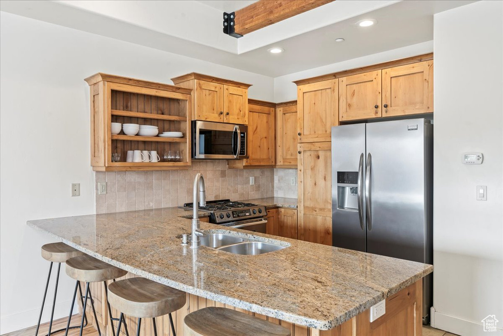 Kitchen featuring kitchen peninsula, light stone countertops, a breakfast bar, stainless steel appliances, and tasteful backsplash
