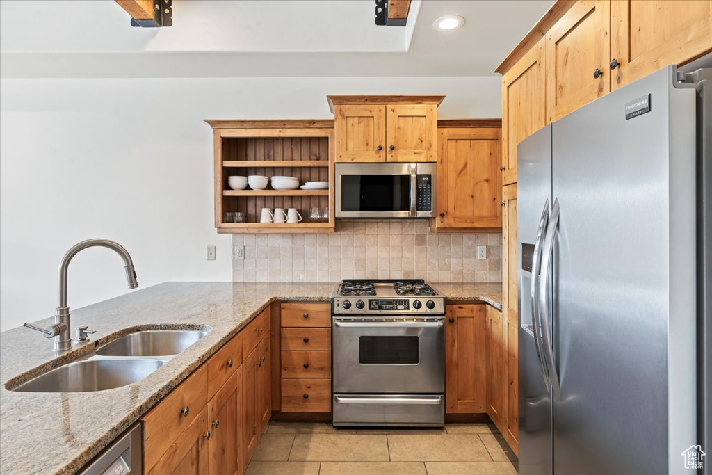 Kitchen with appliances with stainless steel finishes, light stone counters, tasteful backsplash, light tile floors, and sink