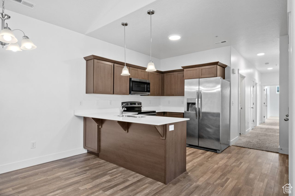 Kitchen with appliances with stainless steel finishes, hanging light fixtures, wood-type flooring, kitchen peninsula, and a chandelier