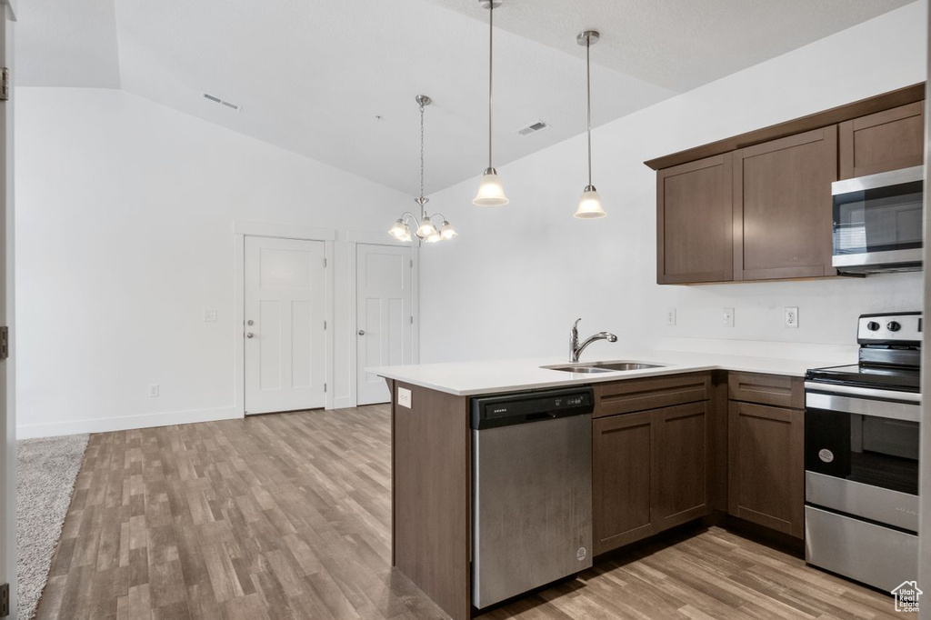 Kitchen featuring stainless steel appliances, a notable chandelier, vaulted ceiling, sink, and light hardwood / wood-style flooring