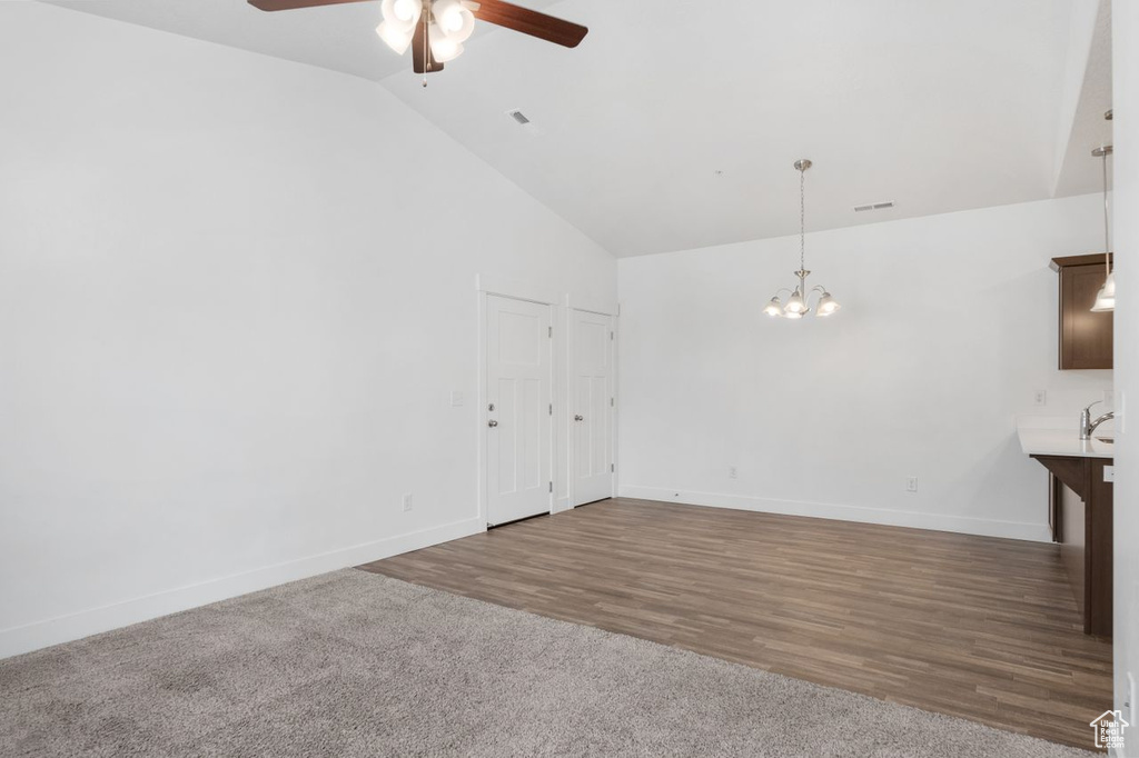 Empty room with high vaulted ceiling, dark hardwood / wood-style floors, and ceiling fan with notable chandelier