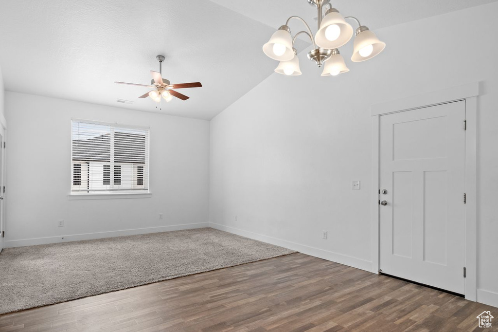 Carpeted empty room featuring ceiling fan with notable chandelier and lofted ceiling