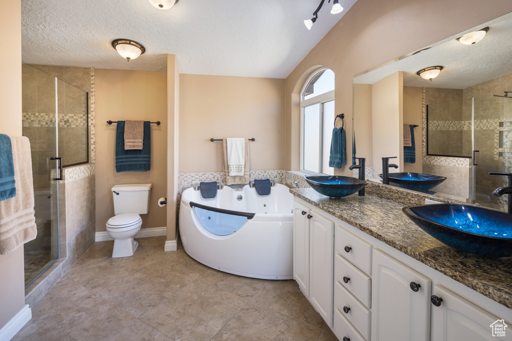 Full bathroom featuring toilet, vanity with extensive cabinet space, double sink, a textured ceiling, and tile floors