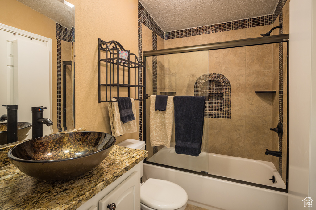 Full bathroom with toilet, enclosed tub / shower combo, large vanity, and a textured ceiling