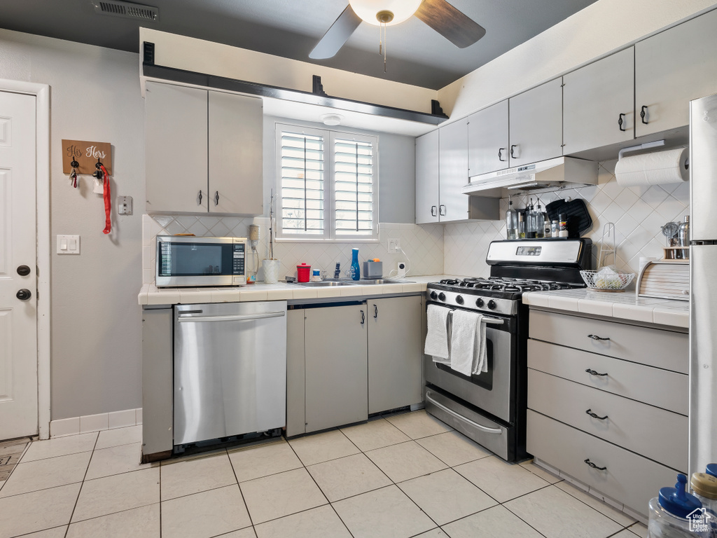 Kitchen featuring backsplash, stainless steel appliances, ceiling fan, and tile countertops