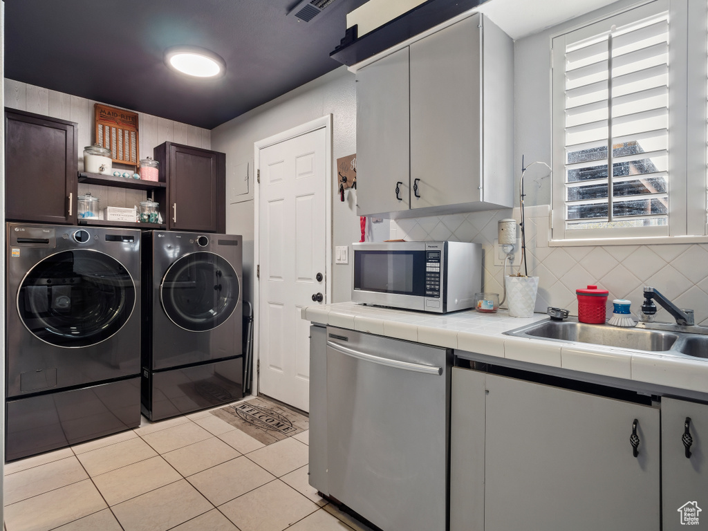 Laundry room with washer and dryer, light tile floors, and sink