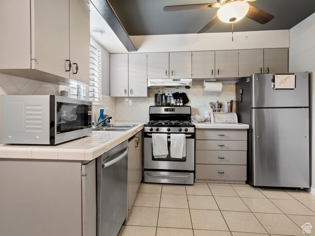 Kitchen featuring tile countertops, backsplash, ceiling fan, and stainless steel appliances