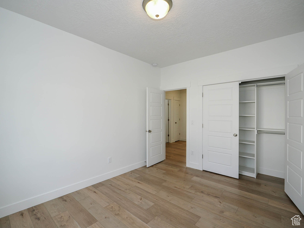 Unfurnished bedroom featuring a textured ceiling, a closet, and hardwood / wood-style flooring