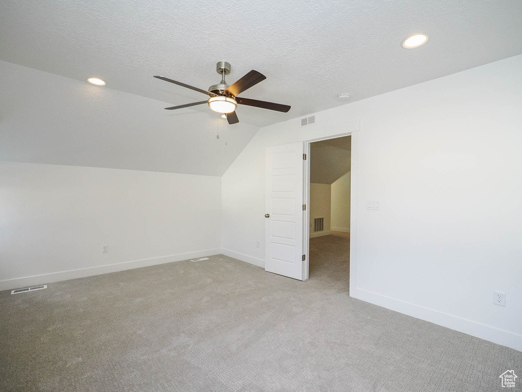 Additional living space featuring ceiling fan, light carpet, vaulted ceiling, and a textured ceiling