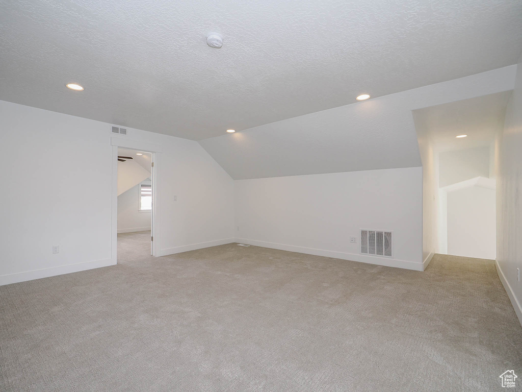 Bonus room featuring a textured ceiling, light colored carpet, and vaulted ceiling