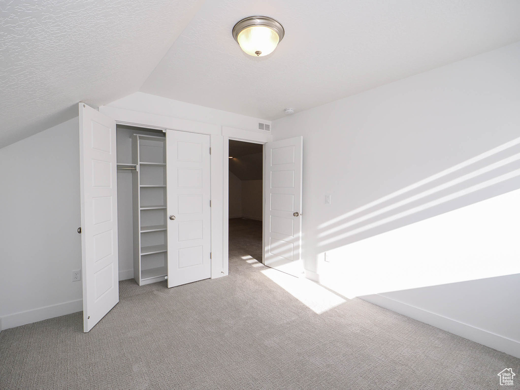 Unfurnished bedroom featuring light carpet, a textured ceiling, a closet, and vaulted ceiling