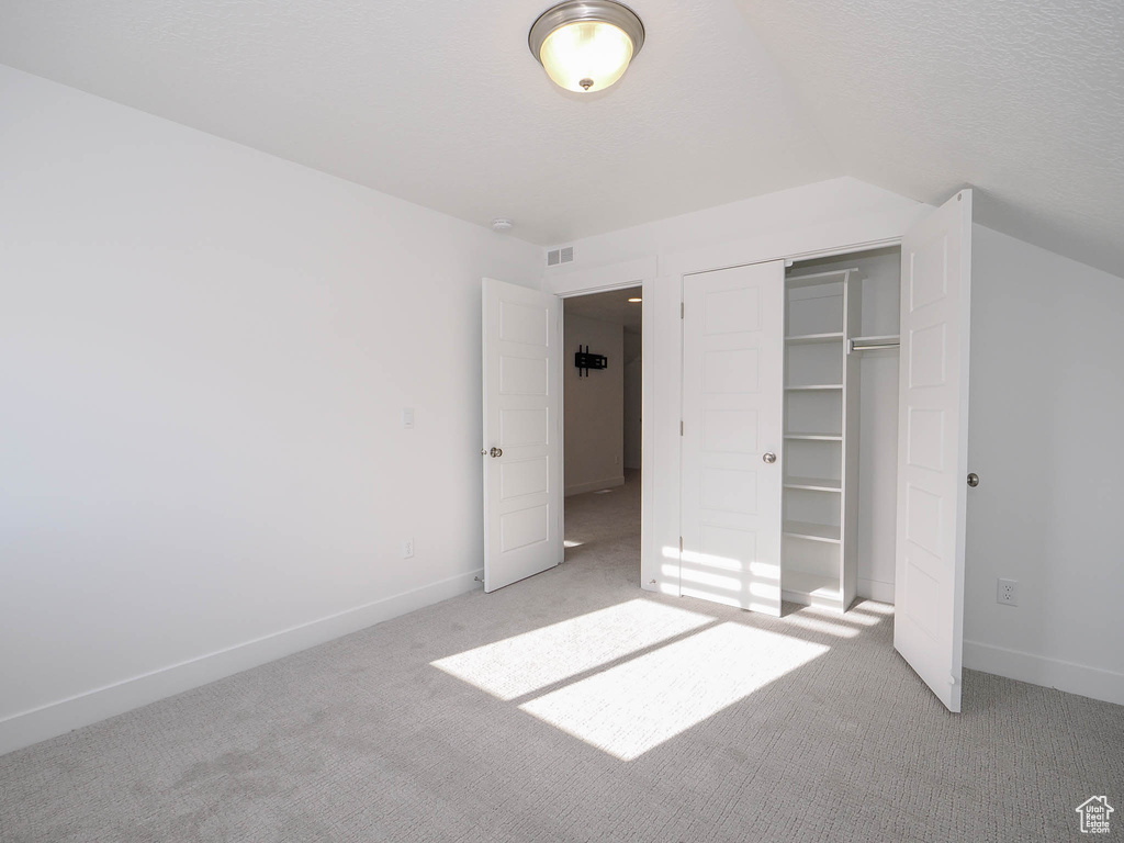 Unfurnished bedroom with light carpet, a closet, and vaulted ceiling