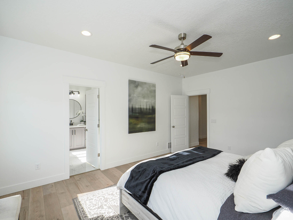 Bedroom with ensuite bath, light hardwood / wood-style floors, and ceiling fan
