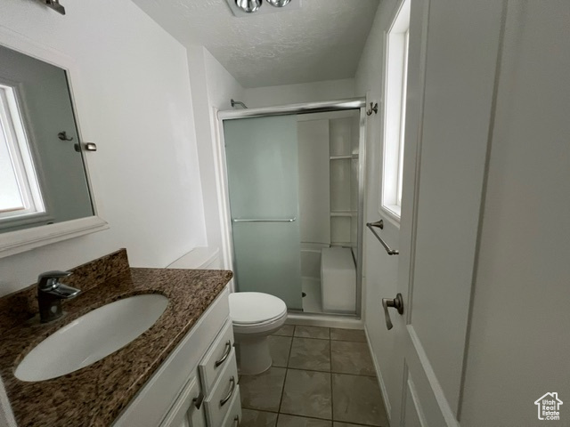 Bathroom featuring an enclosed shower, vanity, tile flooring, toilet, and a textured ceiling