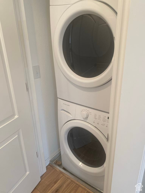 Clothes washing area featuring stacked washer and dryer and wood-type flooring