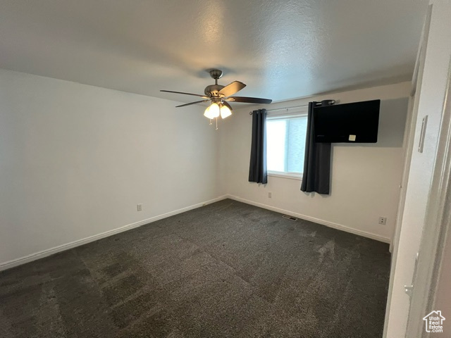 Empty room featuring dark colored carpet and ceiling fan