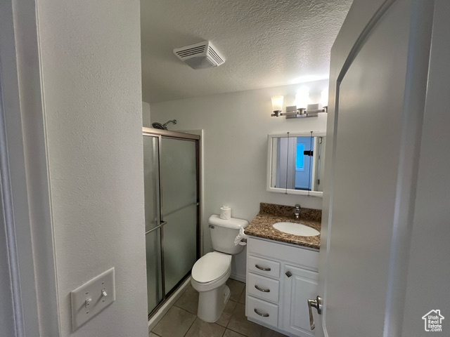 Bathroom with tile flooring, a textured ceiling, an enclosed shower, toilet, and vanity