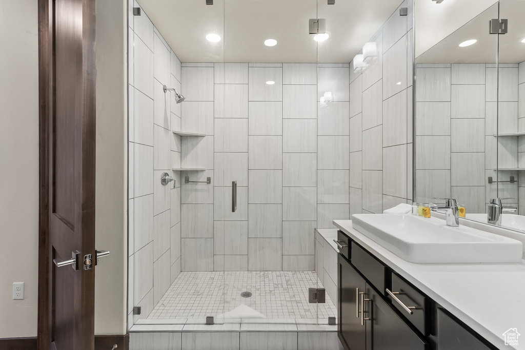 Bathroom featuring a shower with shower door, vanity, and tile walls