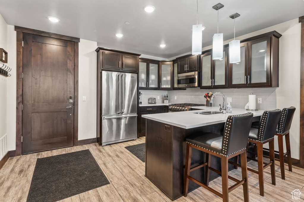 Kitchen with appliances with stainless steel finishes, light hardwood / wood-style flooring, dark brown cabinets, and hanging light fixtures