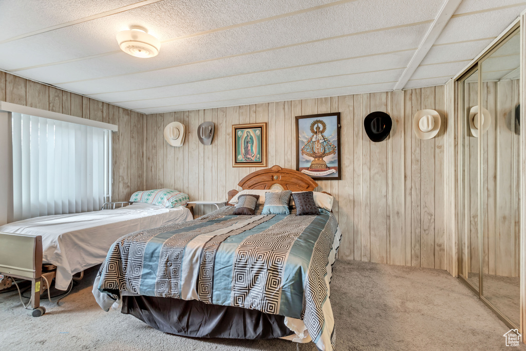Carpeted bedroom featuring wooden walls and a textured ceiling