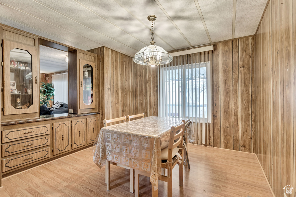 Dining space with an inviting chandelier, wooden walls, and light hardwood / wood-style flooring