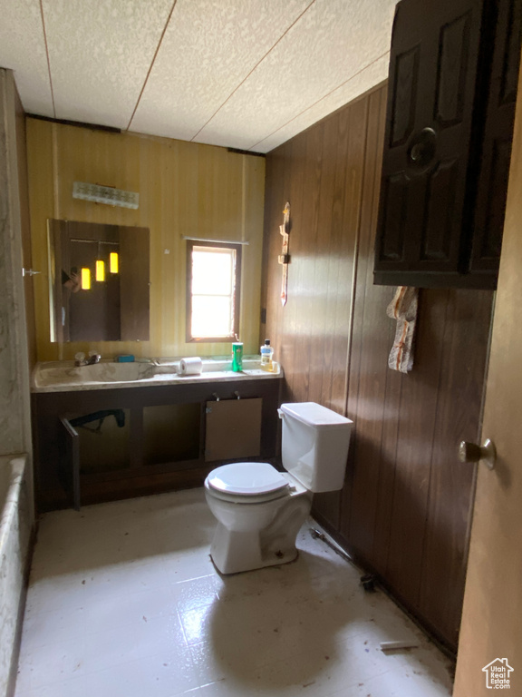 Bathroom with a paneled ceiling, toilet, wood walls, and vanity