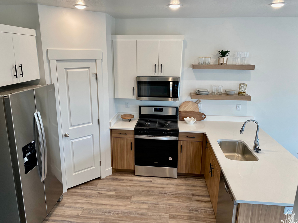 Kitchen featuring stainless steel appliances, sink, white cabinets, and light wood-type flooring