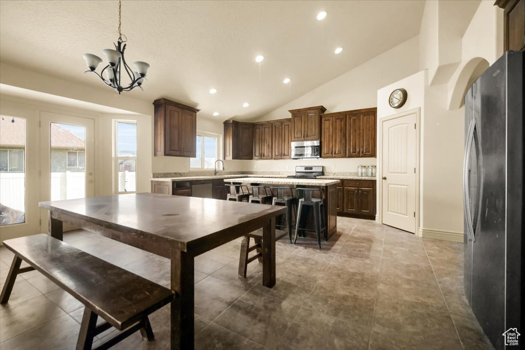 Kitchen with appliances with stainless steel finishes, a kitchen island, a notable chandelier, vaulted ceiling, and decorative light fixtures