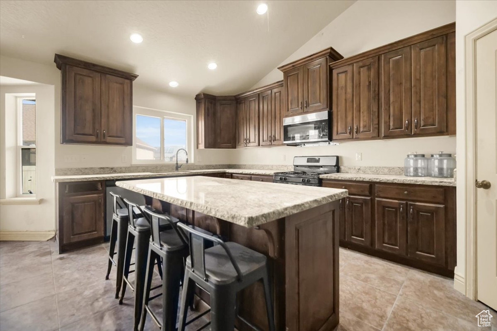 Kitchen with appliances with stainless steel finishes, vaulted ceiling, a center island, and light tile floors