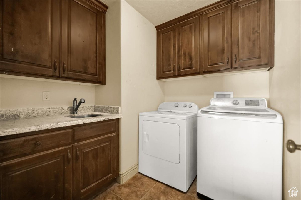 Clothes washing area featuring dark tile flooring, sink, cabinets, washer and dryer, and hookup for a washing machine